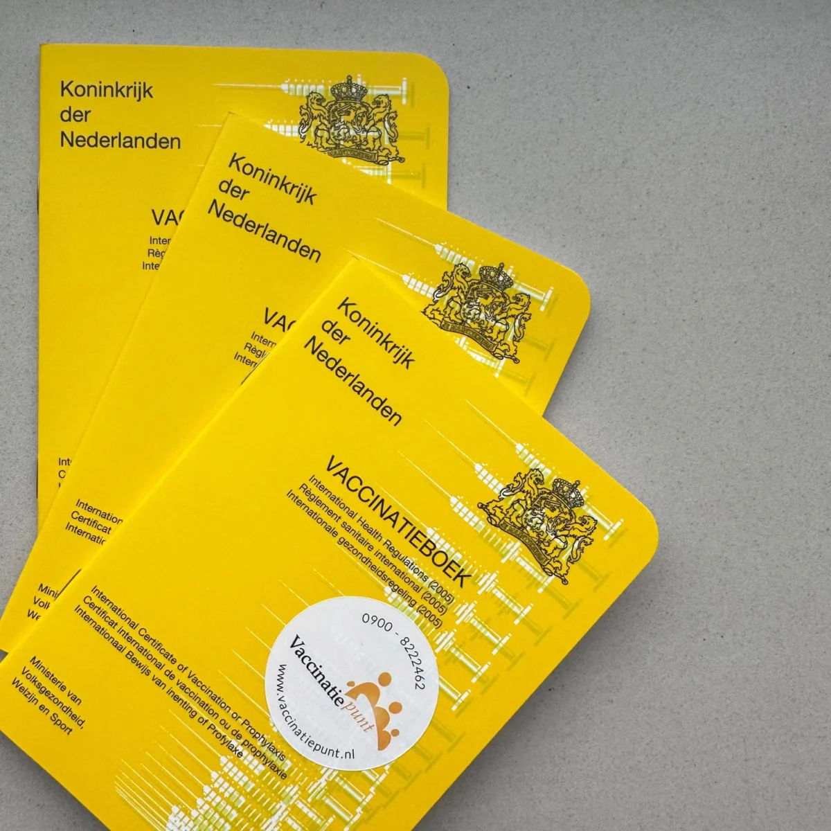 Three bright yellow Dutch vaccination booklets stacked diagonally on a gray surface.