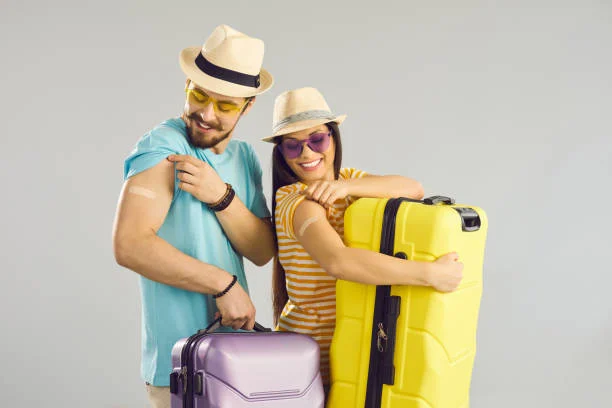 A couple with suitcases showing off adhesive bandages on their upper arms.