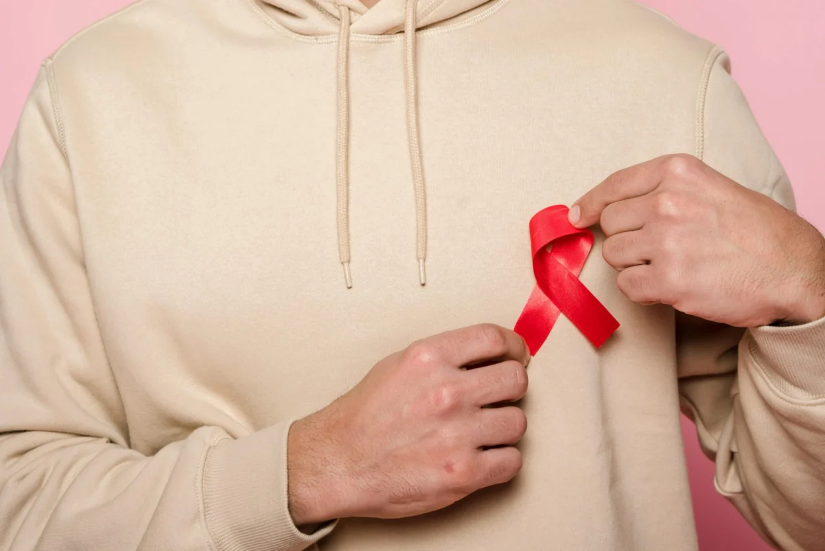 Person in a beige hoodie holding a red awareness ribbon on their chest.