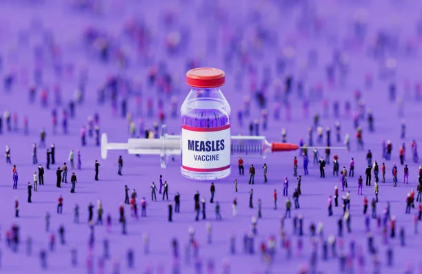 A measles vaccine vial and syringe surrounded by miniature figures on a purple surface.