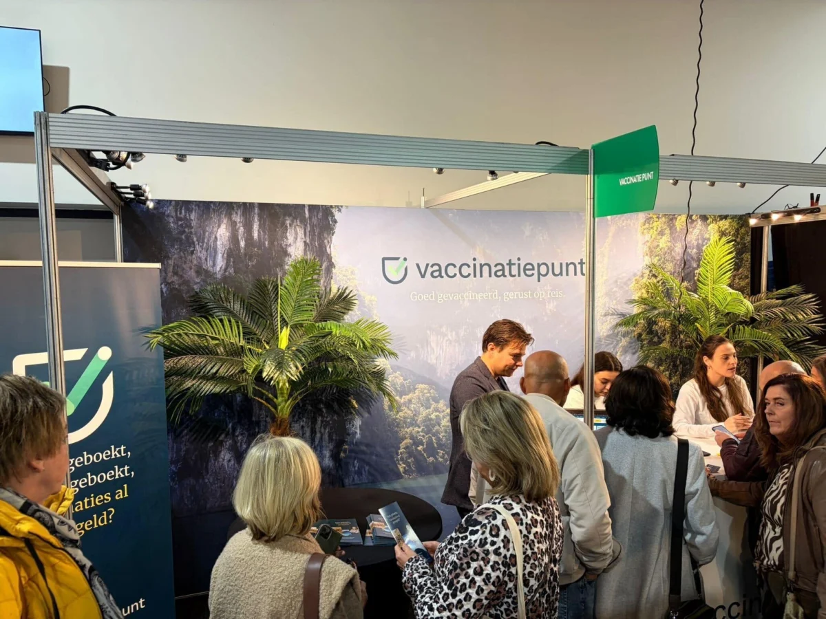 People gathering around a Vaccinatiepunt exhibition booth decorated with tropical imagery.