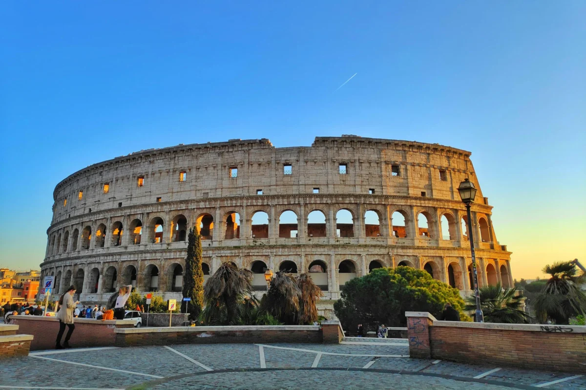 The ancient Roman Colosseum illuminated by sunlight under a clear blue sky in Rome.