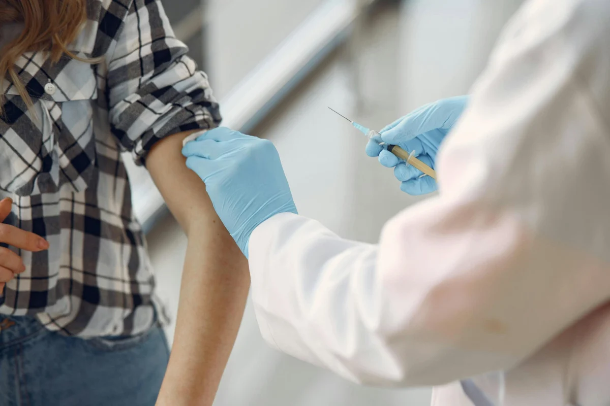 Healthcare worker wearing blue gloves preparing a patient's arm for a vaccine injection.