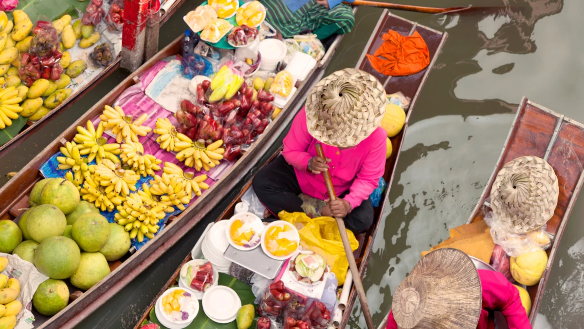 Overhead view of wooden boats filled with fresh tropical fruits at a floating market.