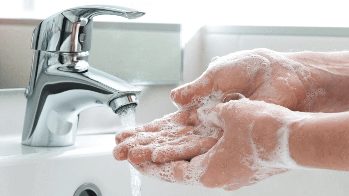 Person washing soapy hands under running water from a chrome sink faucet.