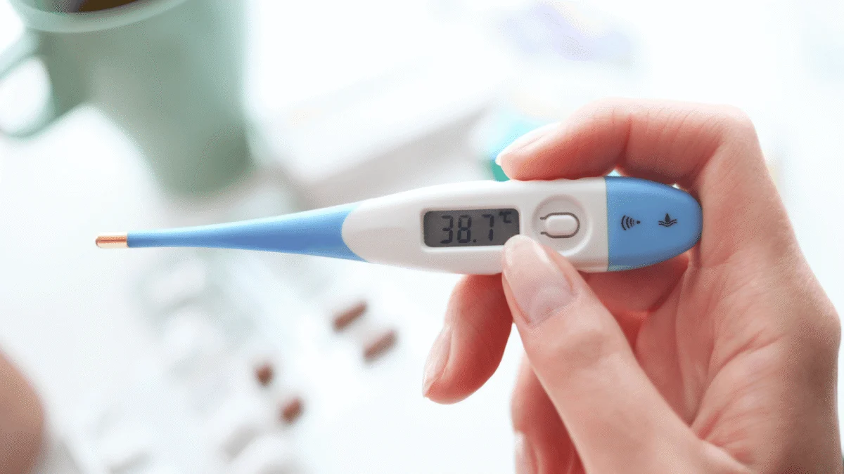 A hand holding a digital thermometer showing a temperature reading of 38.7 degrees Celsius.