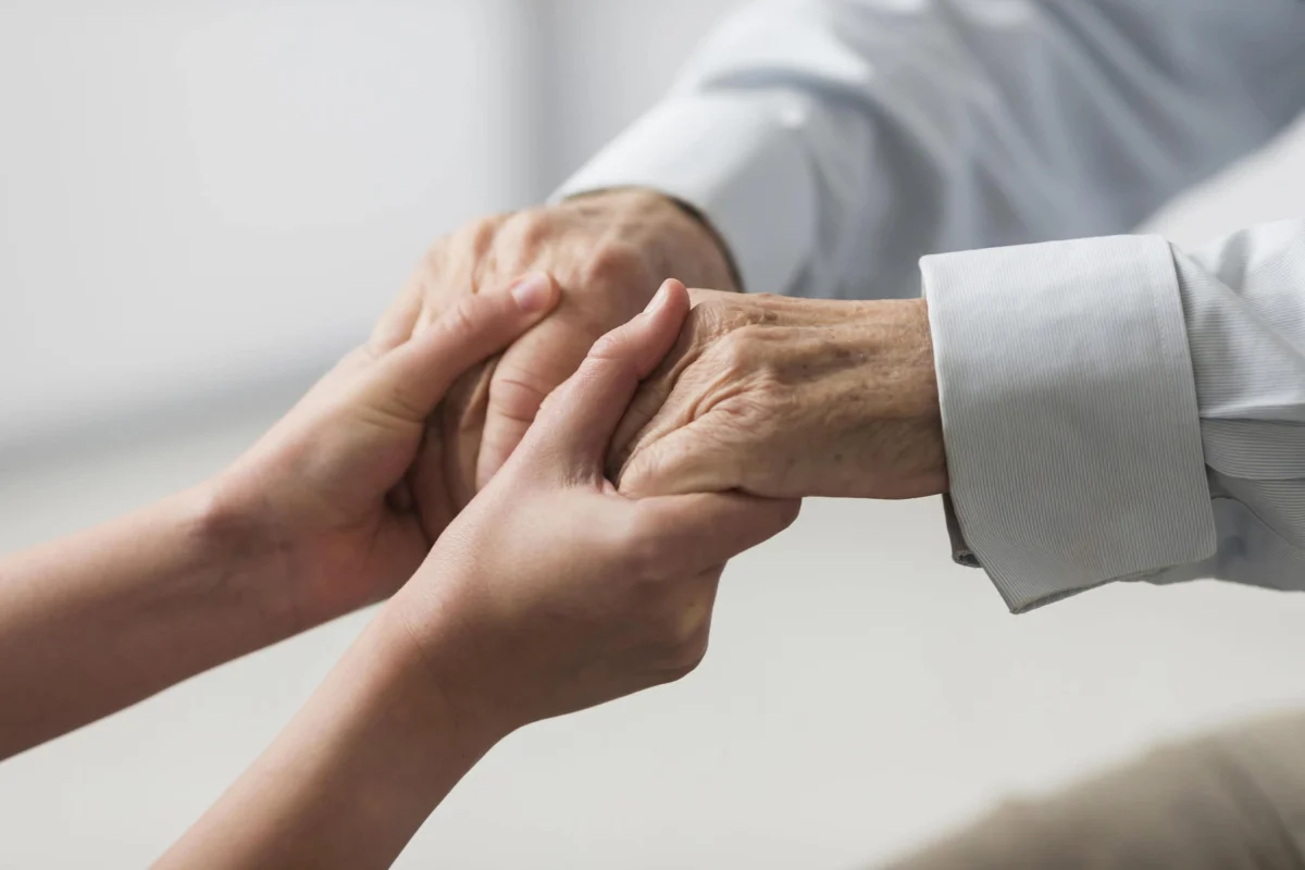 Close-up of a caregiver tenderly holding the wrinkled hands of an elderly person.
