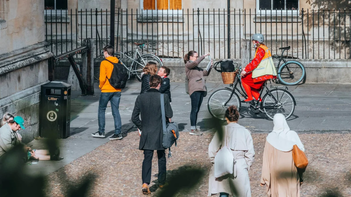 People walking and riding bicycles on a paved cobblestone street outside a building.