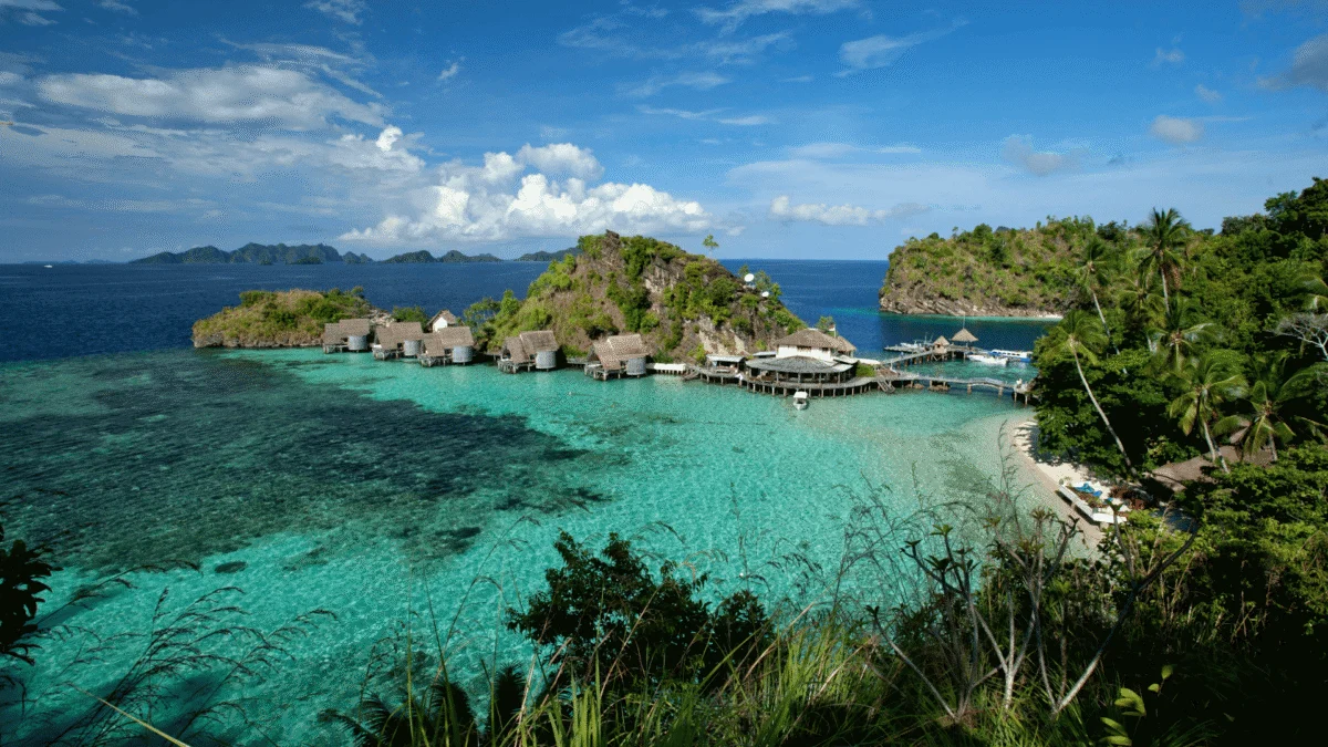 Overwater bungalows situated in clear turquoise water along lush green tropical island hills.
