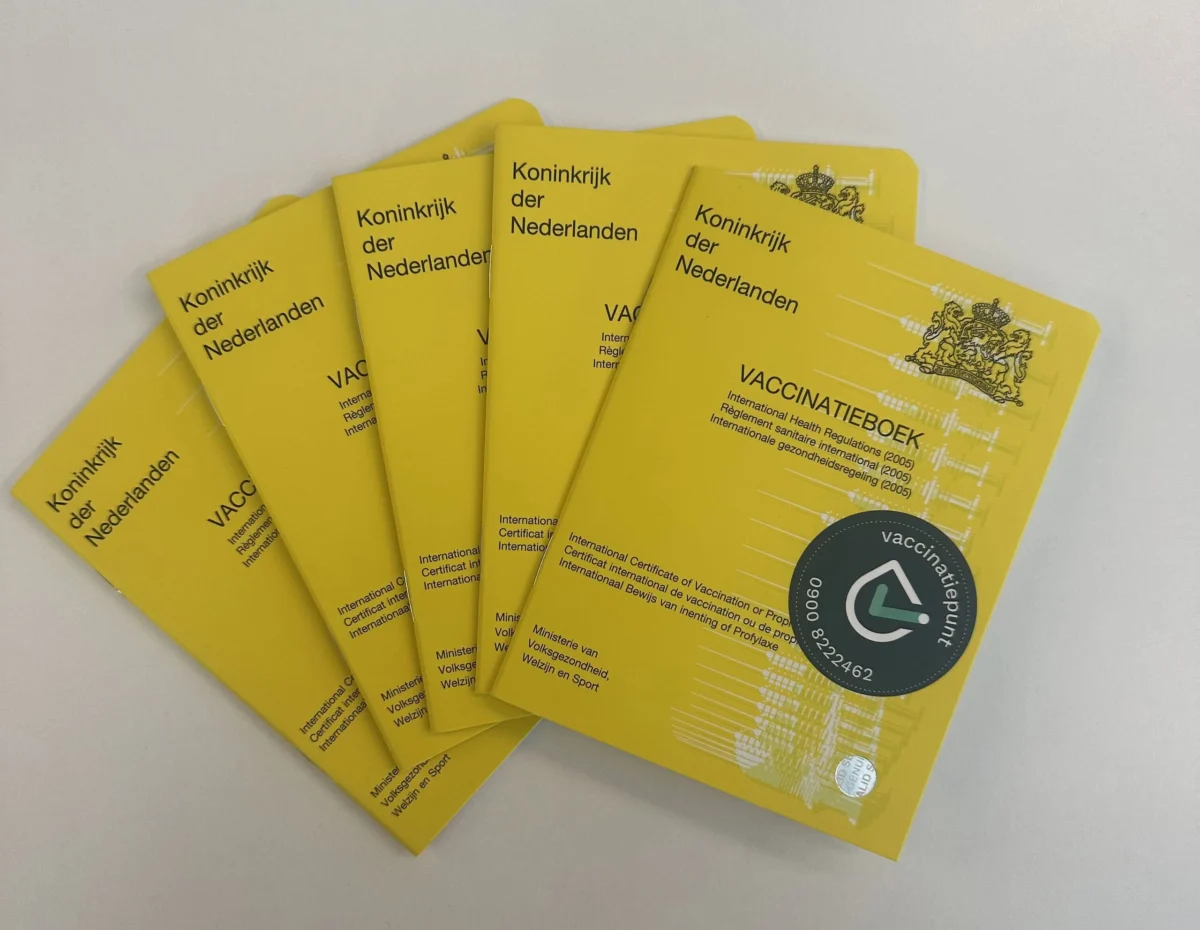 Five yellow Dutch international vaccination booklets fanned out on a white surface.