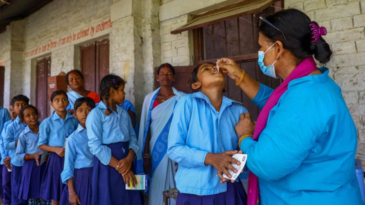 A healthcare worker administers oral vaccine drops to a schoolgirl standing in line.