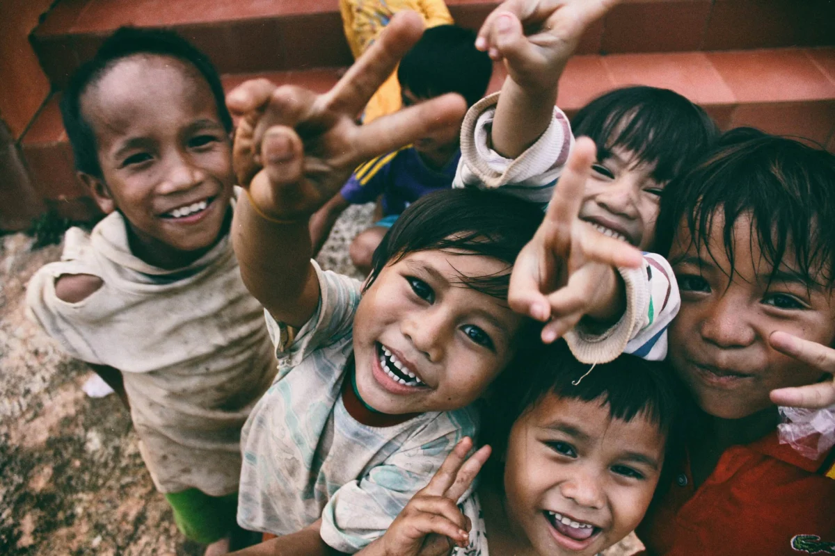 Young, smiling children gathered together, holding up peace signs to the camera.