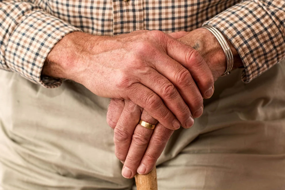 An elderly person's hands resting on top of a wooden walking stick