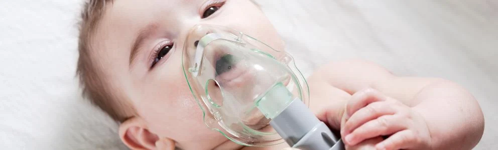 Baby wearing a clear nebulizer mask over their mouth and nose while lying down.