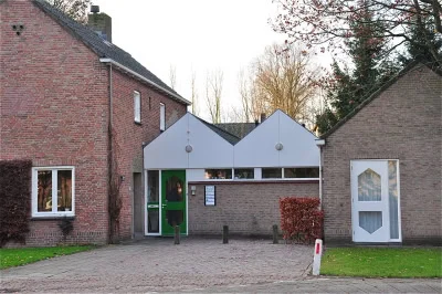 Brick building with a modern white gabled entrance and green door connecting two structures