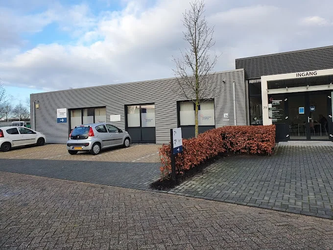 Exterior of a modern grey office building with parked cars outside the entrance.