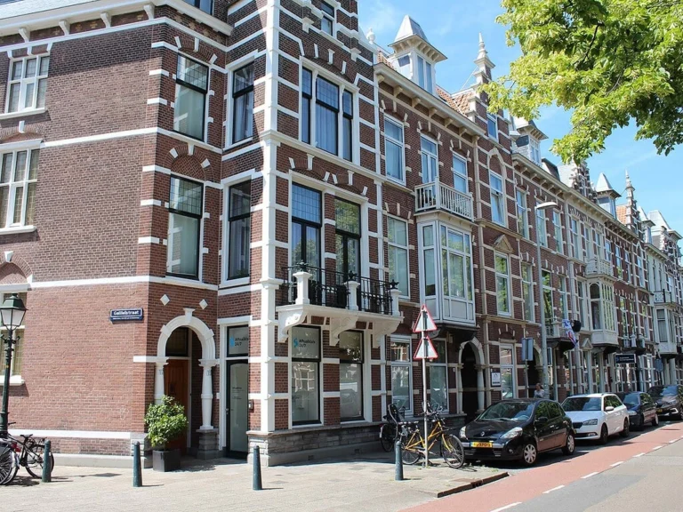 Multi-story red brick Dutch townhouse with ornate white trim on a street corner