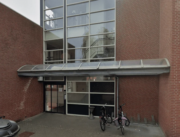 Brick building entrance with a curved canopy, glass facade, and bicycles parked outside