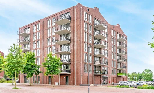 Red brick apartment building with multiple balconies and large windows under a pale blue sky