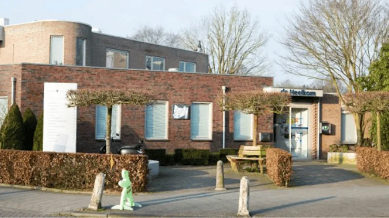 Brick exterior of the De Heelkom health center with entrance and trimmed trees.