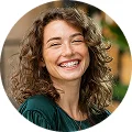 Smiling woman with curly brown hair wearing a dark green top