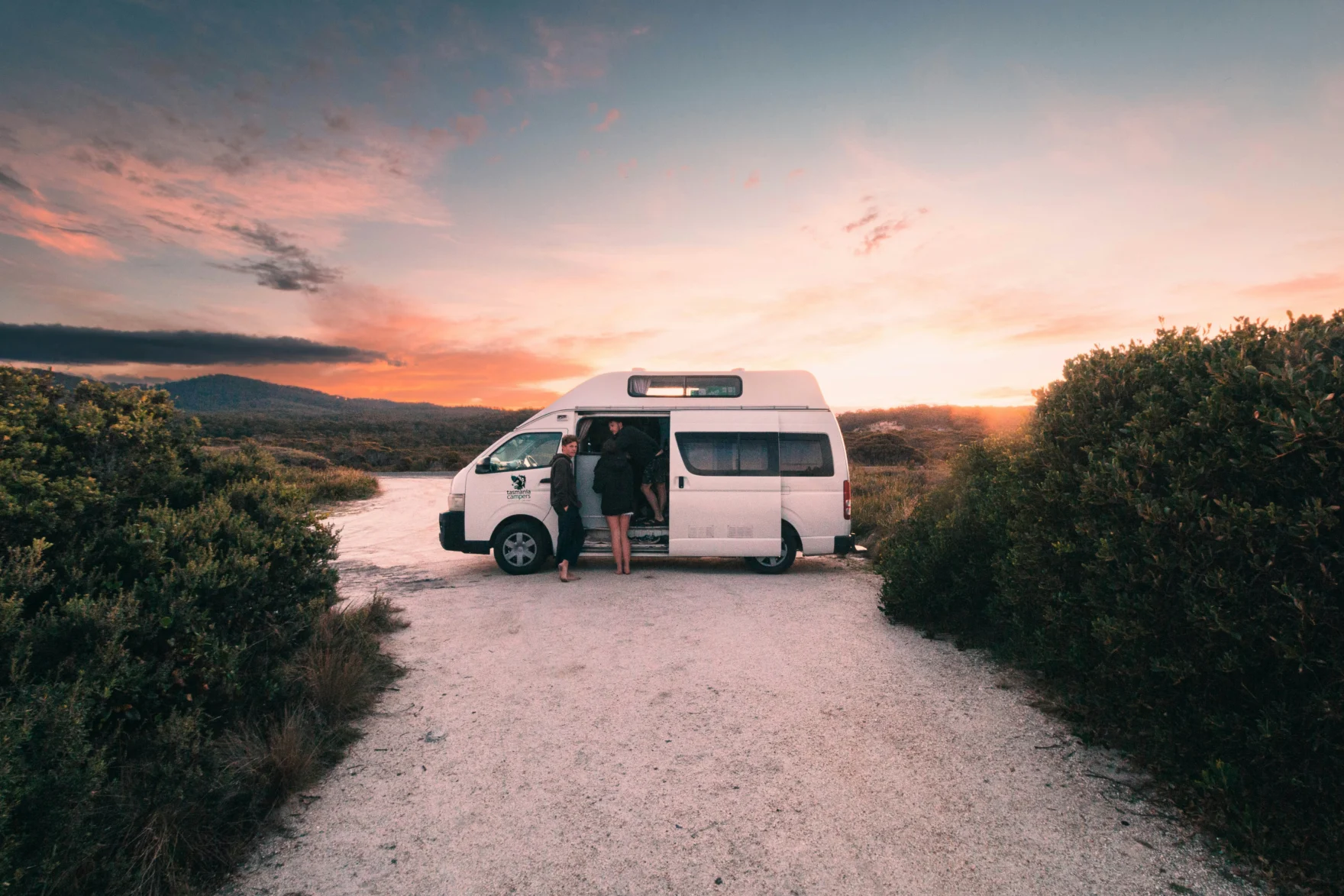 Campervan op een zandpad bij zonsondergang