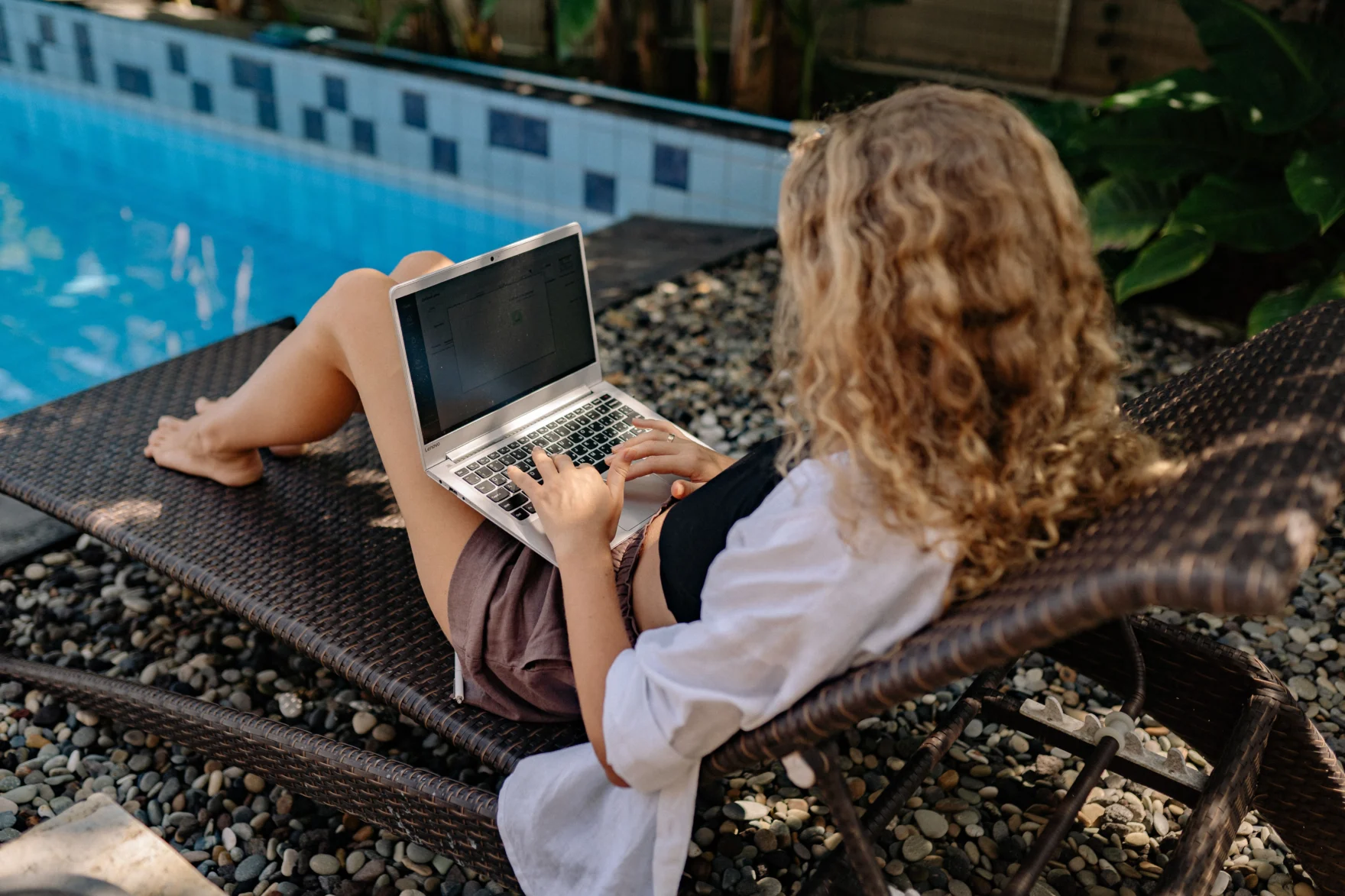 Vrouw werkt op haar laptop op een ligbed bij een zwembad