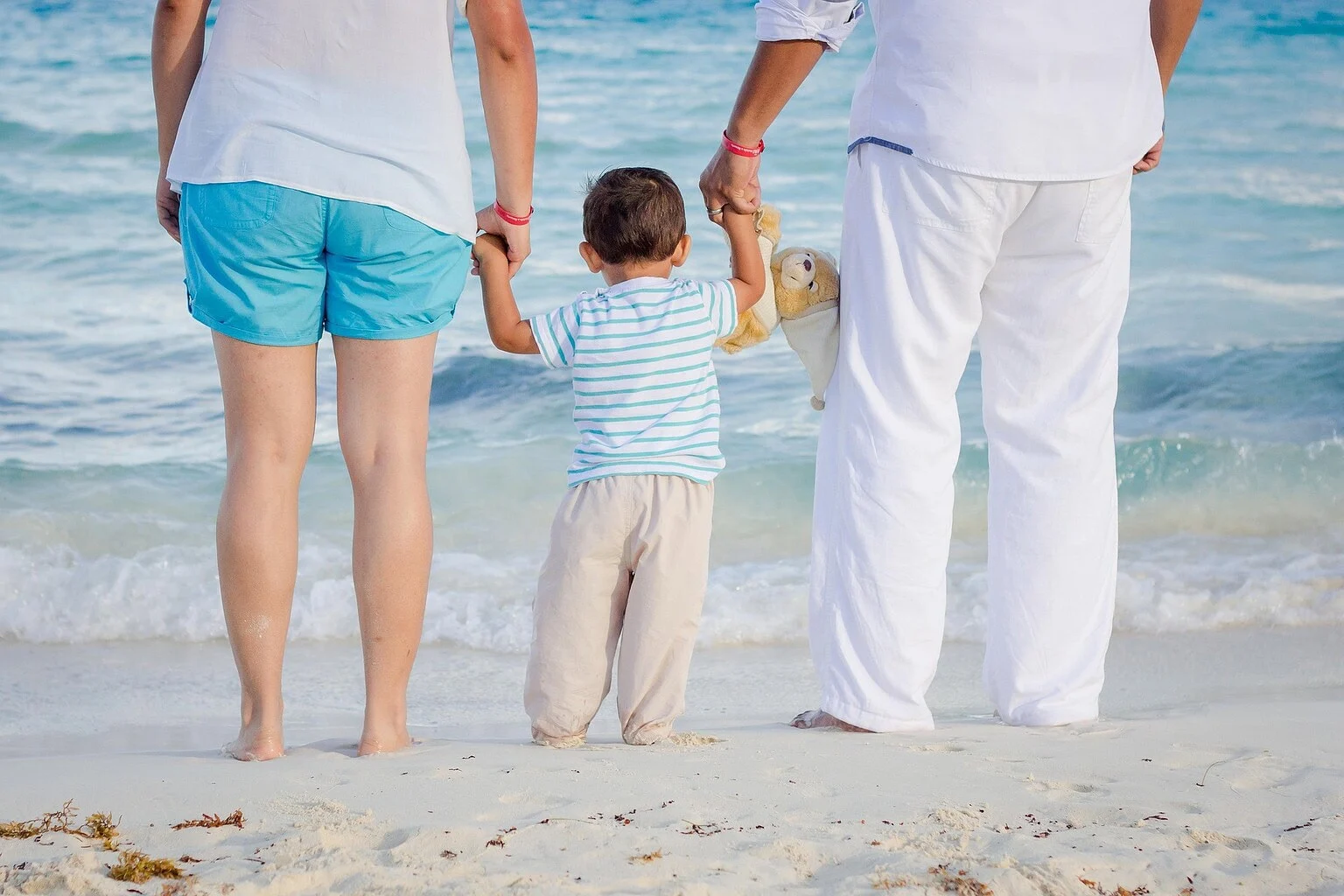 Ouders lopen hand in hand met hun kind door de branding