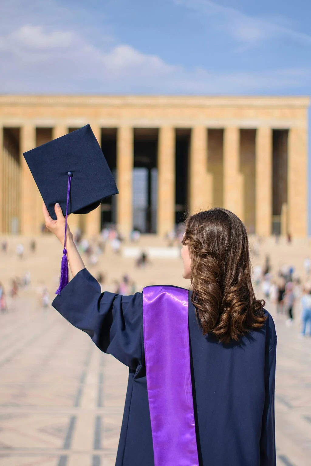 Afgestudeerde gooit haar baret omhoog voor een universiteitsgebouw