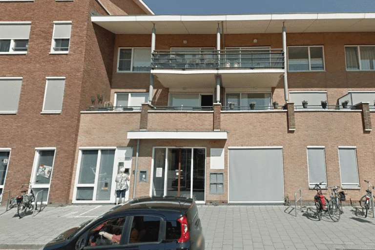 Modern brick apartment building entrance with balconies, parked bicycles, and a car in front