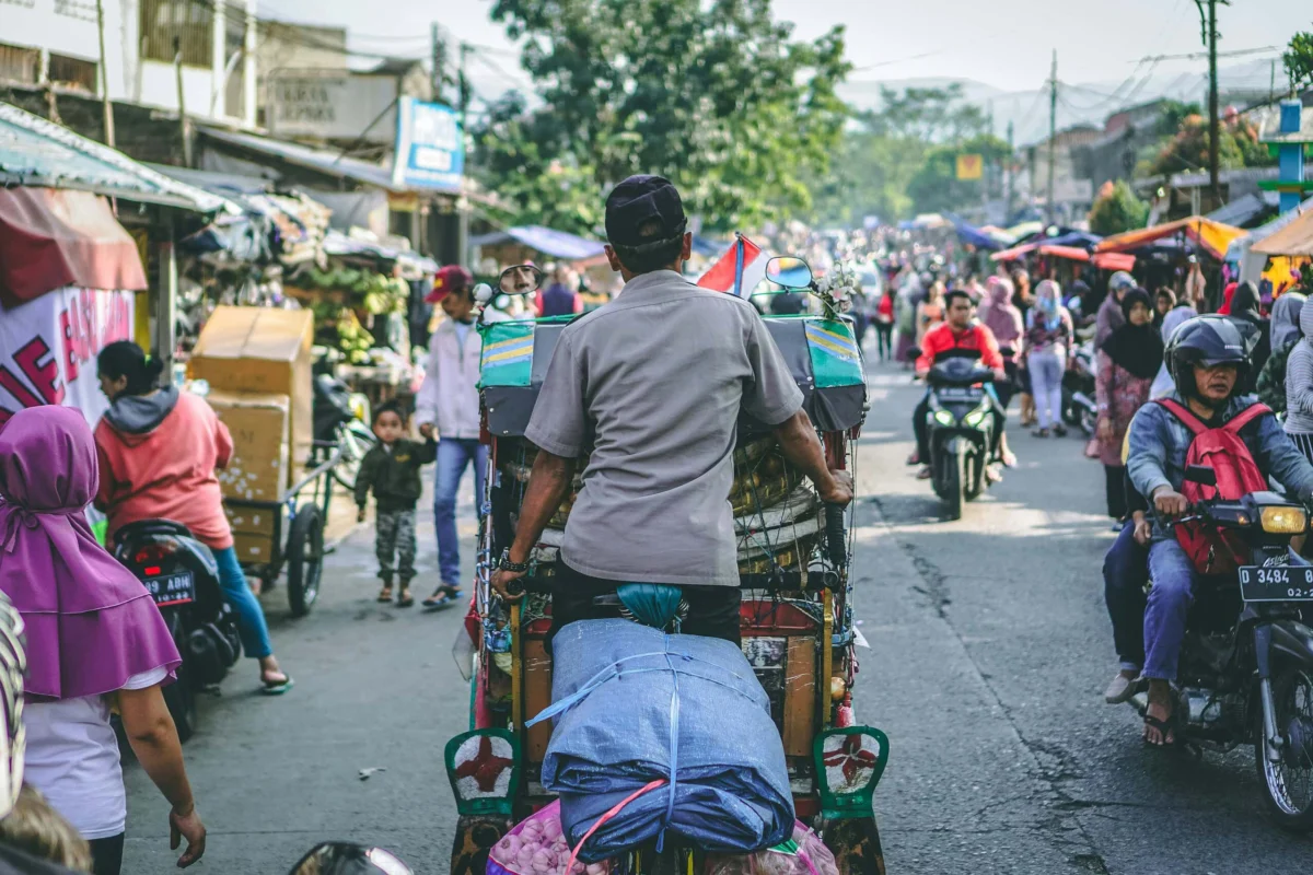 A pedicab driver navigating a bustling street market crowded with motorbikes and pedestrians.