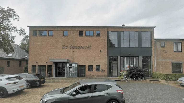 Exterior of the brick De Eendracht building with cars parked in front