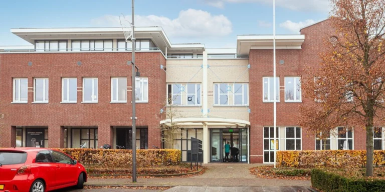 Red brick building exterior with a central entrance canopy and walkway in Bergeijk