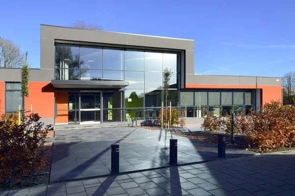 Modern office building with large glass windows, orange and grey facade, and paved entrance.