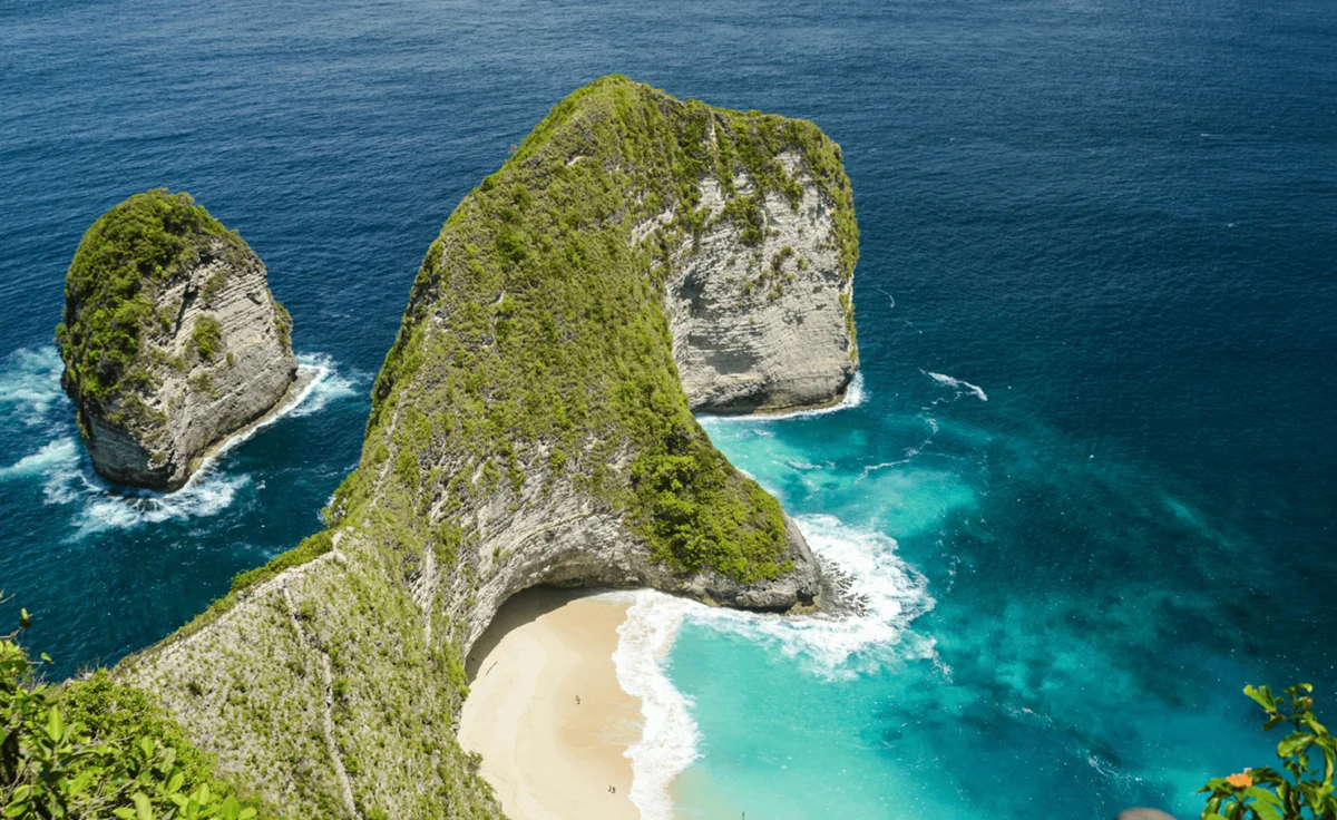 Lush green cliff overlooking a secluded sandy beach and vibrant turquoise ocean water