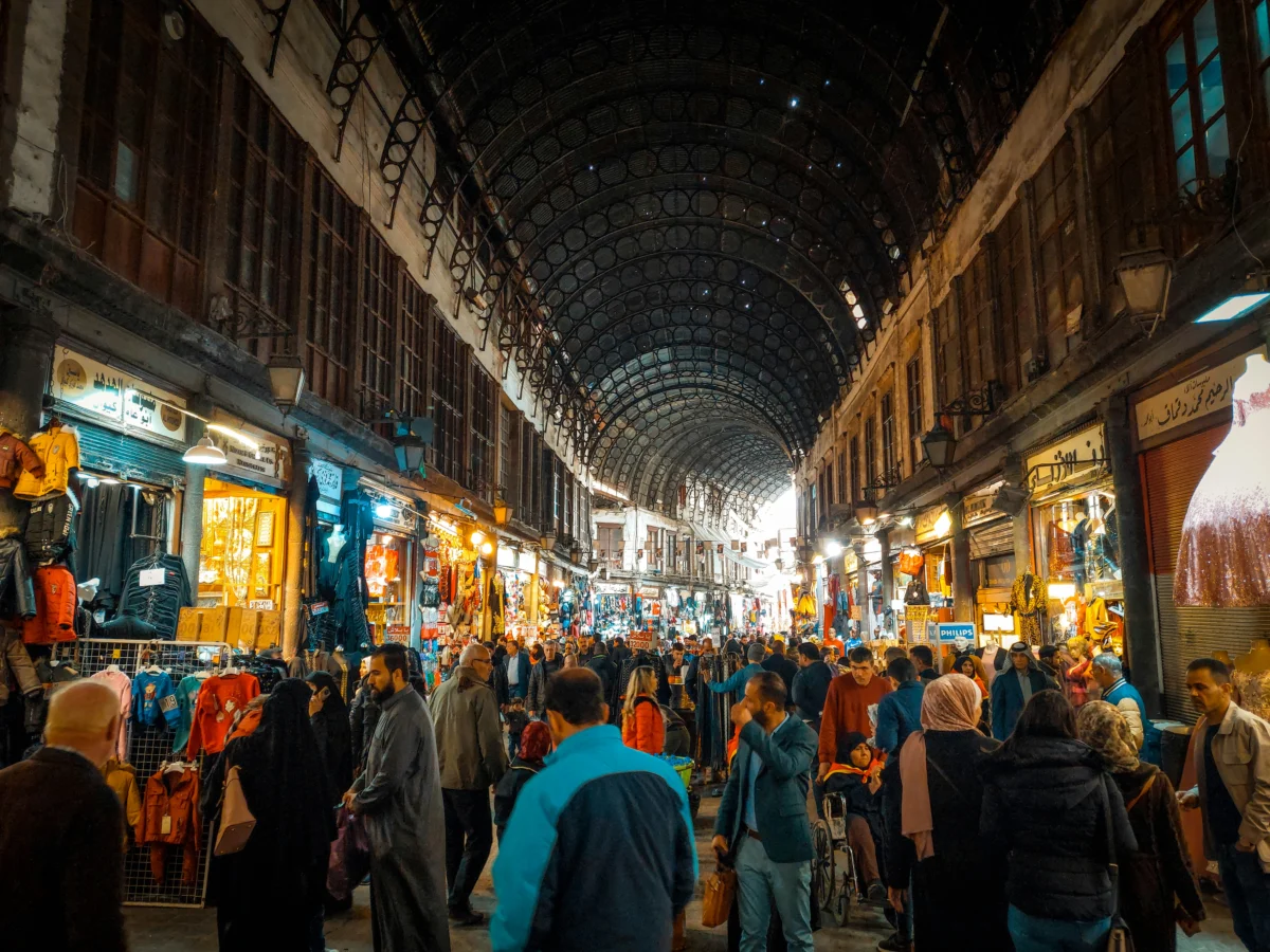 People walking through the bustling Al-Hamidiyah Souq lined with illuminated shops in Damascus.