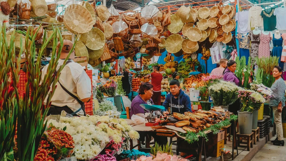 Vendors surrounded by fresh flowers and hanging woven baskets at a vibrant indoor market