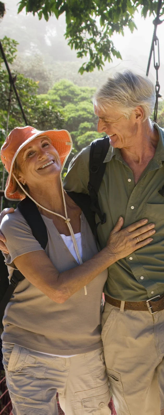 Senior couple smiling and embracing while hiking outdoors through a lush green forest