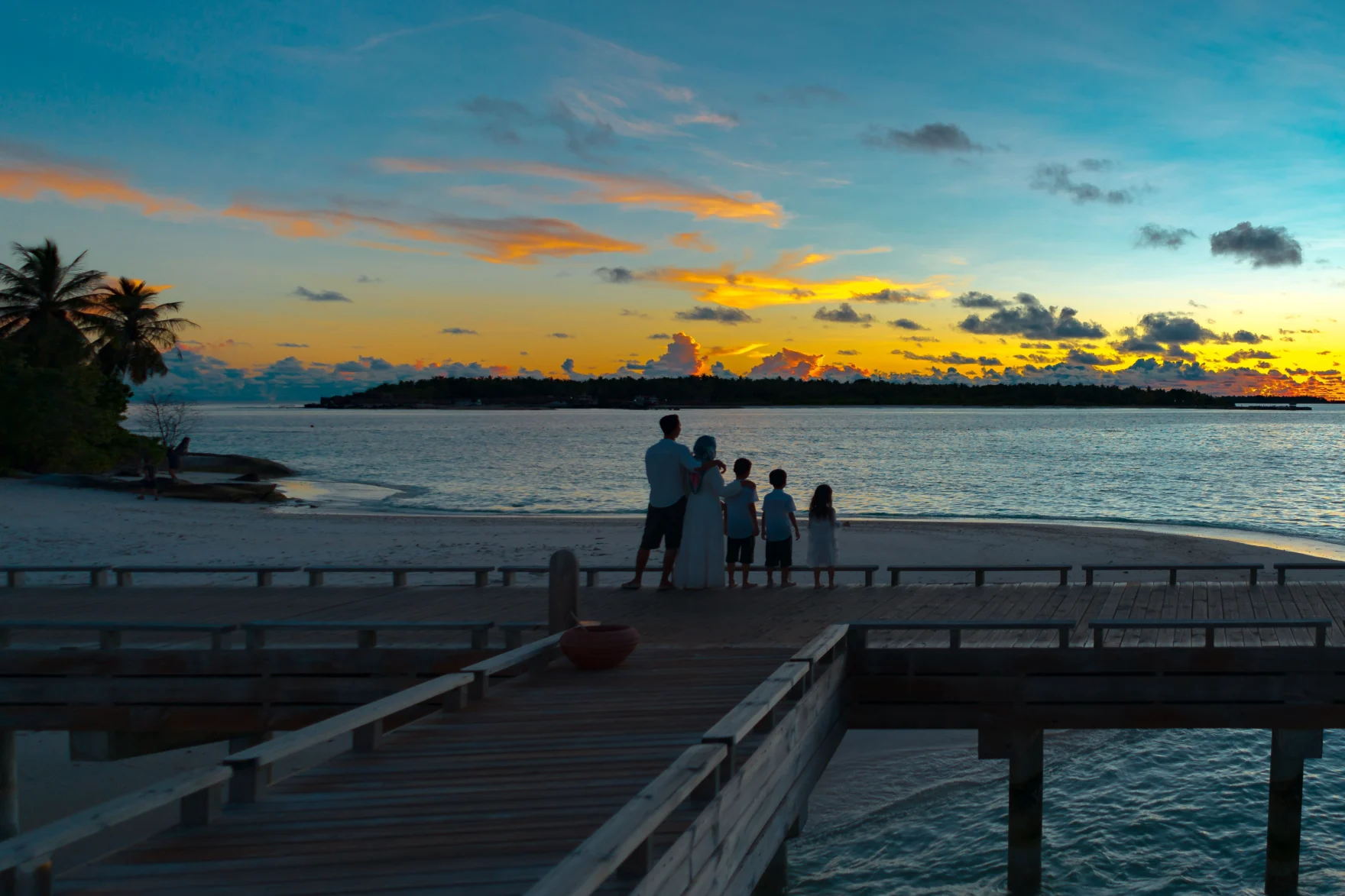 Family standing on a wooden pier watching a vibrant sunset over the ocean