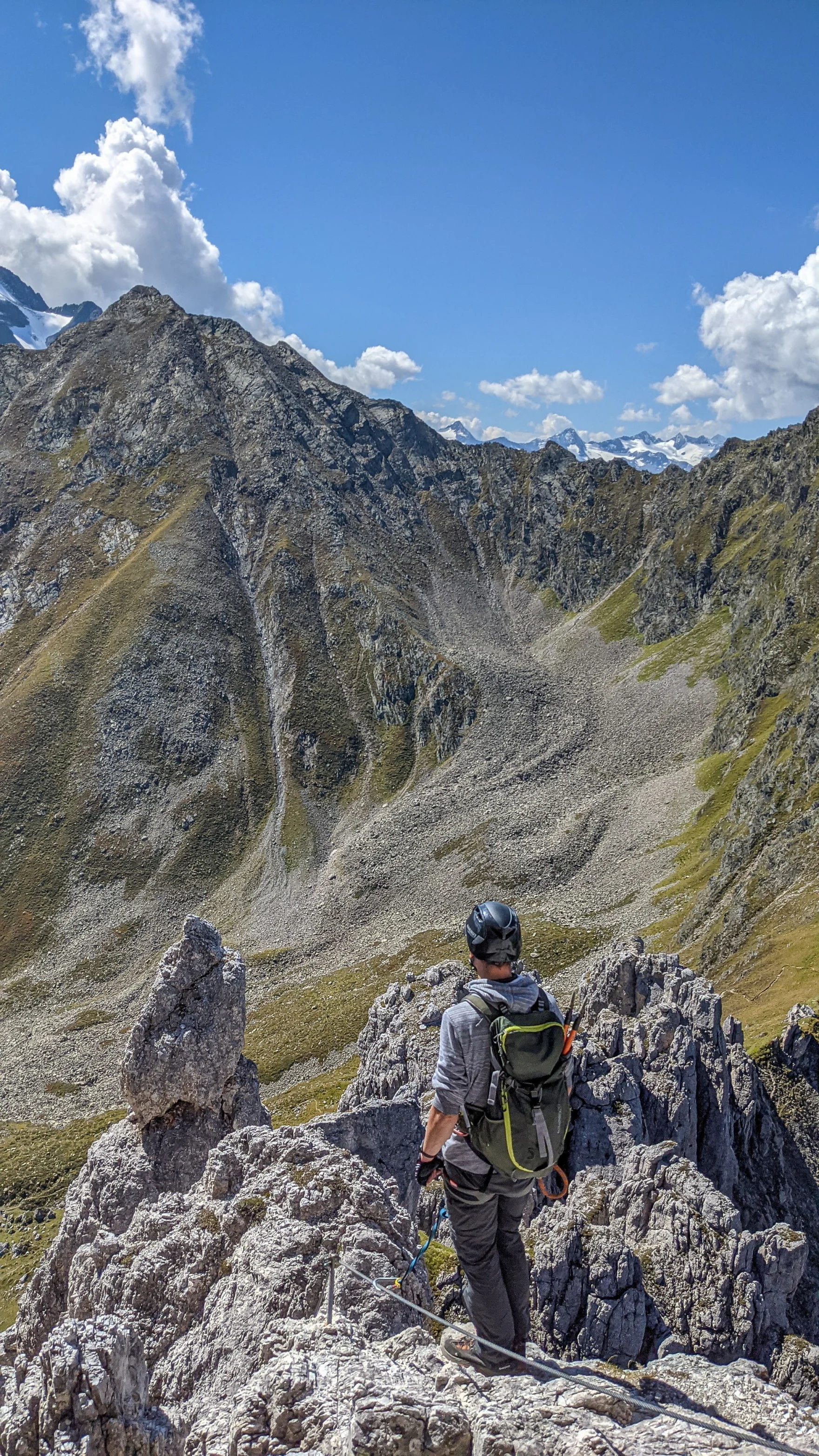 Climber with helmet and backpack standing on a rocky ridge overlooking an alpine valley