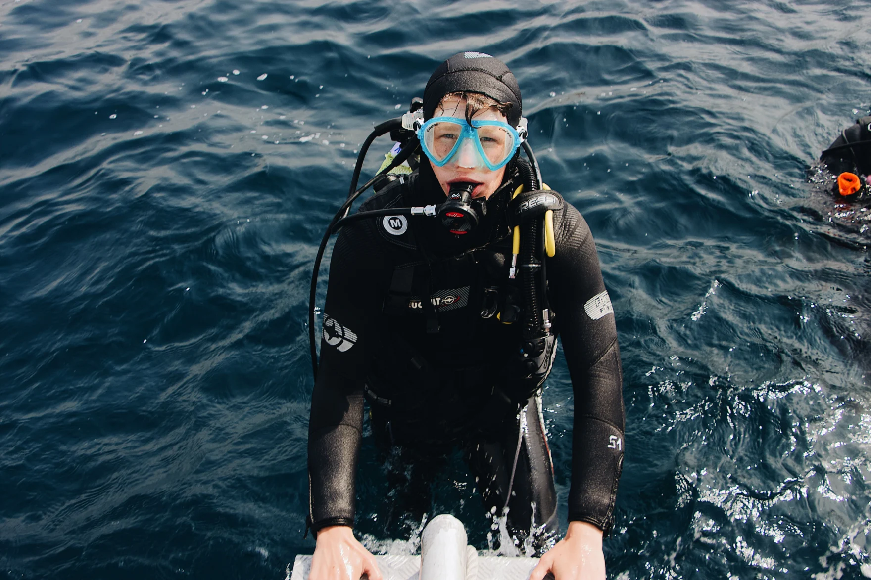 Scuba diver in full gear emerging from the ocean onto a boat ladder