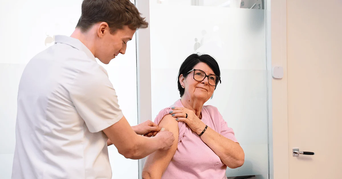 A healthcare worker applies an adhesive bandage to a senior woman's upper arm.