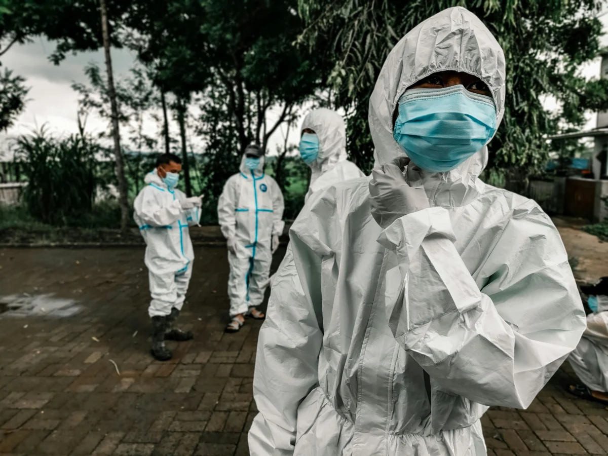 Healthcare workers wearing white protective hazmat suits and blue face masks outdoors.