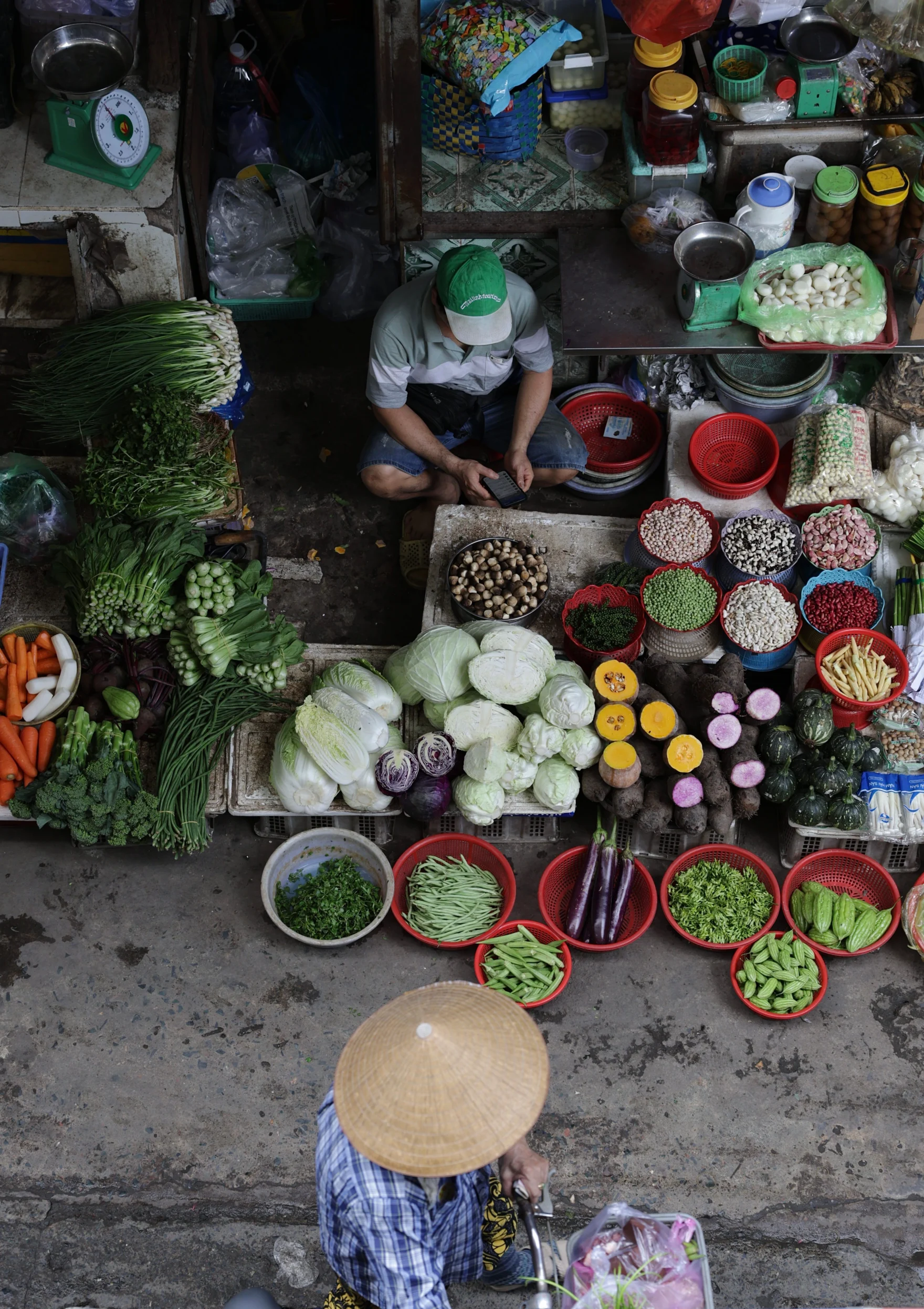 Overhead view of an outdoor market stall with colorful fresh vegetables and a seated vendor