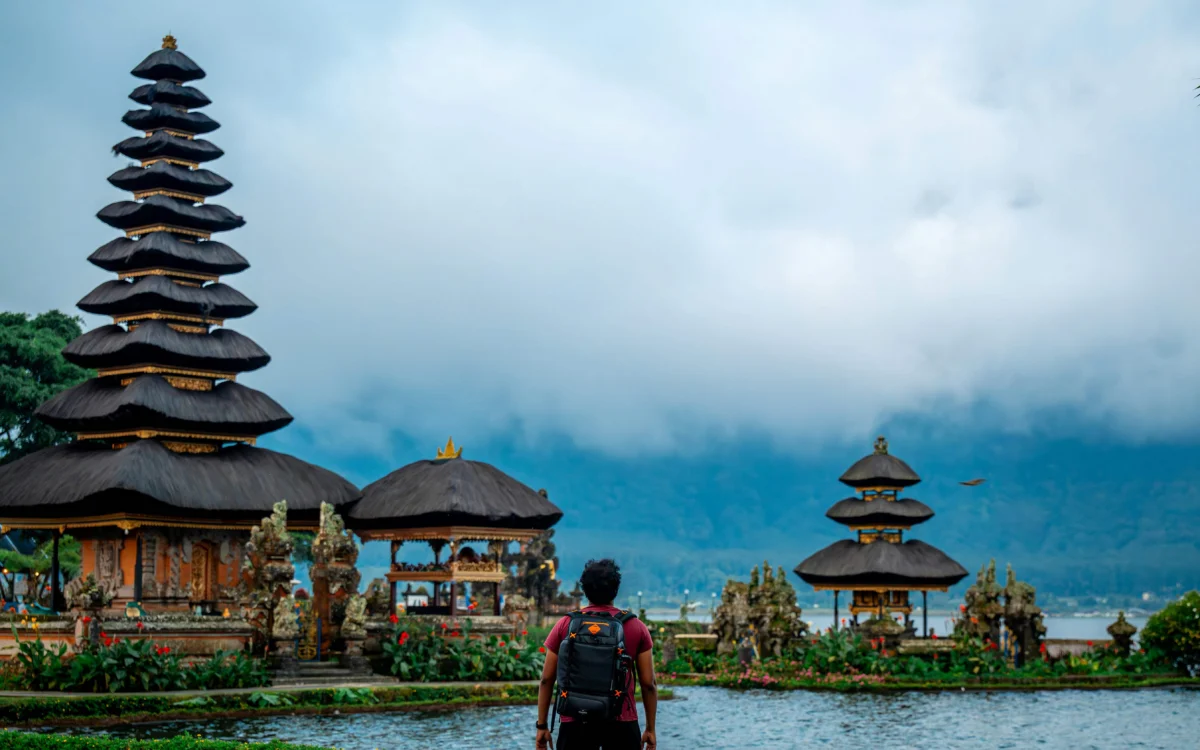 Traveler with a backpack looking at the Ulun Danu Beratan temple across a misty lake